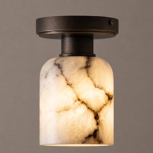May include: A flush mount ceiling light fitting featuring a cylindrical white stone shade with dark grey veining. The shade is attached to a circular, dark bronze-toned metal base that mounts directly to the ceiling surface for a low profile.
