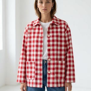 May include: A long-sleeve button-down jacket featuring a red and white gingham check pattern, a classic collar, and two large square patch pockets on the front. The garment is worn over a plain white t-shirt and blue denim jeans.