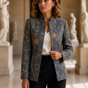 May include: A charcoal grey blazer featuring a mandarin collar and an intricate embroidered floral vine pattern in shades of gold, orange, and green. The blazer is worn over a simple white camisole and paired with solid black trousers.
