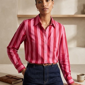 Peut inclure: Une chemise à manches longues boutonnée avec des rayures verticales alternant des tons rose vif et rouge foncé. La chemise présente un col classique, une poche poitrine sur le côté gauche et des poignets boutonnés, portée avec un jean bleu foncé.