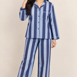 Può includere: Un set pigiama a due pezzi composto da una camicia a maniche lunghe con bottoni e pantaloni abbinati. Il set presenta righe verticali in tonalità alternate di blu navy scuro e azzurro, rifinito con profili bianchi lungo il colletto, i polsini, la tasca e l'abbottonatura frontale.