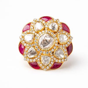 Puede incluir: Un anillo de oro con un gran diamante central de talla rosa rodeado por un halo de diamantes más pequeños, acentuado por pétalos exteriores de rubíes de color rojo intenso y un borde de diminutos diamantes blancos en pavé floral.