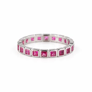 Puede incluir: Una sortija de eternidad en tono plateado que presenta una hilera continua de piedras preciosas de color rosa vibrante con corte cuadrado, engastadas en un canal de metal pulido. El anillo muestra un diseño uniforme y estructurado.