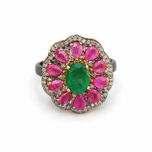 May include: A ring featuring a central oval green gemstone surrounded by a halo of pear-shaped pink rubies. The floral-shaped setting is accented with small white pavé diamonds set in gold, mounted on a smooth, dark, solid-colored band.