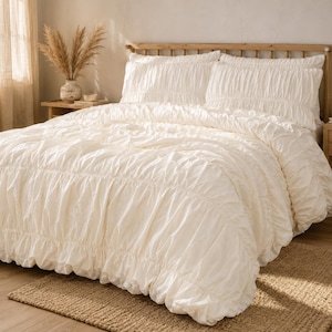 Può includere: Un set di biancheria da letto color crema composto da un copripiumino e due federe abbinate, tutti caratterizzati da una texture arricciata che crea strati orizzontali a balze sull'intera superficie del tessuto per un aspetto strutturato.