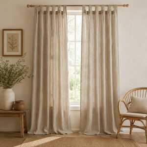 May include: A pair of floor-length, light beige curtains with a textured weave, featuring a tab-top header design. The curtains hang from a wooden rod, covering a window and displaying a semi-sheer quality that allows soft light to filter through.