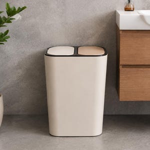 May include: A rectangular dual-compartment trash can with a cream-colored body and a black rim. The top features two separate hinged lids, one in a light cream shade and the other in a metallic bronze finish, designed for waste separation.