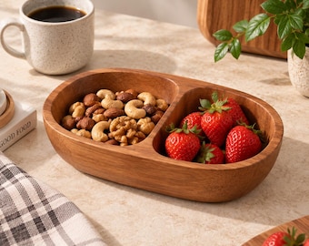 Könnte beinhalten: Eine ovale Servierschale aus Holz mit zwei getrennten Fächern. Eine Seite ist mit einer Mischung aus Nüssen gefüllt, darunter Cashews, Walnüsse und Mandeln. Die andere Seite enthält mehrere frische, leuchtend rote Erdbeeren mit grünen Stielen.