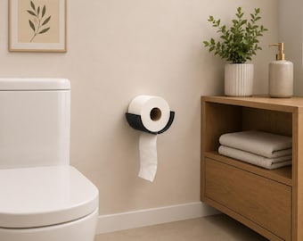 Könnte beinhalten: Ein mattschwarzer, an der Wand montierter Toilettenpapierhalter mit geschwungenem, offenem Design. Der Halter ist sicher an einer hellbeigen Wand befestigt und enthält eine Rolle weißes Toilettenpapier, von der ein Blatt mittig herabhängt.