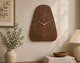 Könnte beinhalten: Eine Wanduhr mit dunkelbrauner Holzmaserung in abgerundeter Trapezform. Das Zifferblatt hat goldfarbene Zeiger und goldfarbene Ziffern an den Positionen 3, 6, 9 und 12 Uhr, während kleine goldene Punkte die übrigen Stunden markieren.