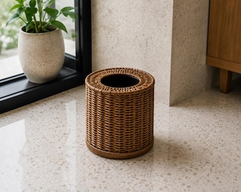 Könnte beinhalten: Ein zylindrischer Taschentuchbox-Bezug mit einer geflochtenen, braunen Rattan-Optik. Der Artikel verfügt über eine kreisförmige Öffnung an der Oberseite und einen festen Boden, passend für eine handelsübliche Taschentuchbox.