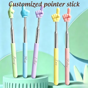 May include: Five telescopic pointer sticks with hand-shaped tips in green, blue, purple, yellow, and pink. Each stick features a silver metal shaft and a colored handle engraved with the names Amy, Mia, Lilly, Leo, and Ruby. Text reads Customized pointer stick.