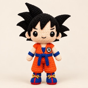May include: A crocheted doll featuring a character with spiky black hair, a light peach complexion, and large black eyes. The doll wears an orange gi with a blue belt, blue wristbands, and blue boots with yellow laces, featuring a circular white emblem.