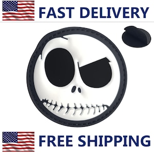 May include: A circular black and white PVC patch featuring a stylized character face with large oval eyes, a small nose, and a wide stitched mouth. The patch has a raised design with a black border and a separate small black circular adhesive backing piece.