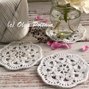 Può includere: Tre tovagliette all'uncinetto bianche su una superficie di legno bianco con un barattolo di vetro di rose bianche e un gomitolo di filo bianco. (c) Olga Poltava