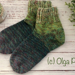 Puede incluir: Un par de calcetines tejidos a mano de color verde, azul y marrón con un ovillo de lana verde, azul y amarillo. Los calcetines tienen un puño de canalé y están colocados sobre una superficie de madera blanca. (c) Olga Poltava