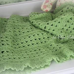 May include: A green crocheted baby blanket with a scalloped edge. The blanket is made with a delicate stitch pattern and is perfect for a baby shower gift.