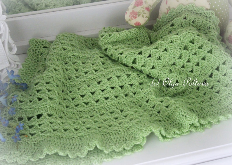May include: A green crocheted baby blanket with a scalloped edge. The blanket is made with a delicate stitch pattern and is perfect for a baby shower gift.