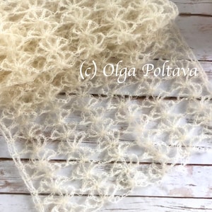 May include: A delicate, off-white crocheted shawl with a lacy, floral pattern. The shawl is laid out on a light wood surface. (c) Olga Poltava