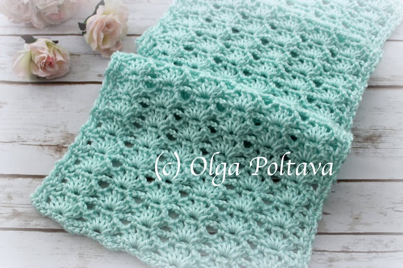 May include: A light blue crocheted scarf with a delicate, lacy pattern. The scarf is folded in half and lying on a white wooden surface. (c) Olga Poltava