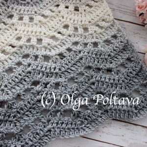 Puede incluir: Un chal tejido a crochet con un degradado de blanco a gris. El chal tiene un patrón de encaje y está hecho con un hilo suave. El chal está sobre una superficie de madera blanca. (c) Olga Poltava