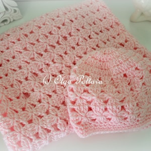 May include: A pink crocheted baby blanket and matching hat. The blanket and hat are made with a delicate flower pattern.
