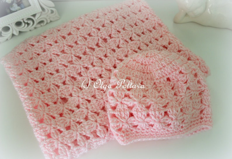 May include: A pink crocheted baby blanket and matching hat. The blanket and hat are made with a delicate flower pattern.