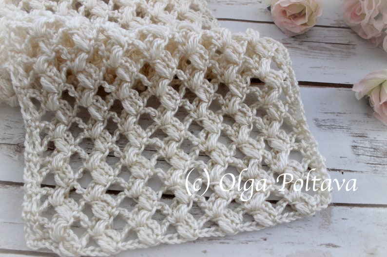 May include: A cream-coloured, hand-crocheted scarf with a delicate openwork pattern. The scarf features a repeating floral-like design and a textured, three-dimensional effect. The image includes the text "(c) Olga Poltava".