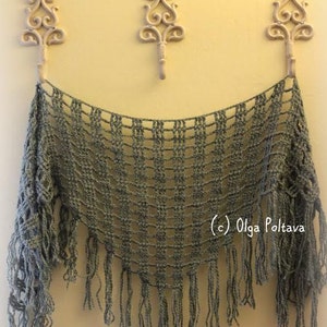 May include: A gray crocheted shawl with fringe hanging from the bottom edge. The shawl is draped over three decorative hooks on a yellow wall.