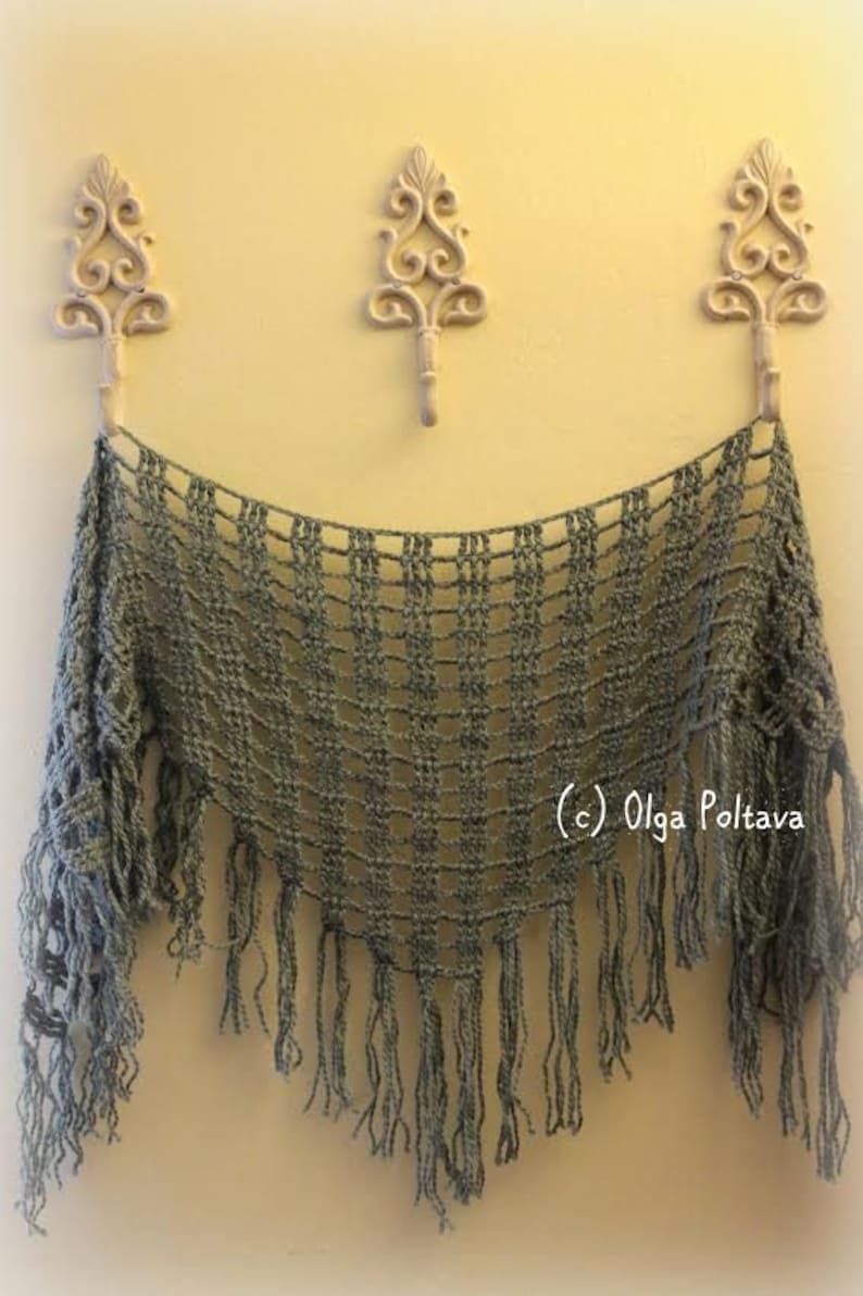 May include: A gray crocheted shawl with fringe hanging from the bottom edge. The shawl is draped over three decorative hooks on a yellow wall.