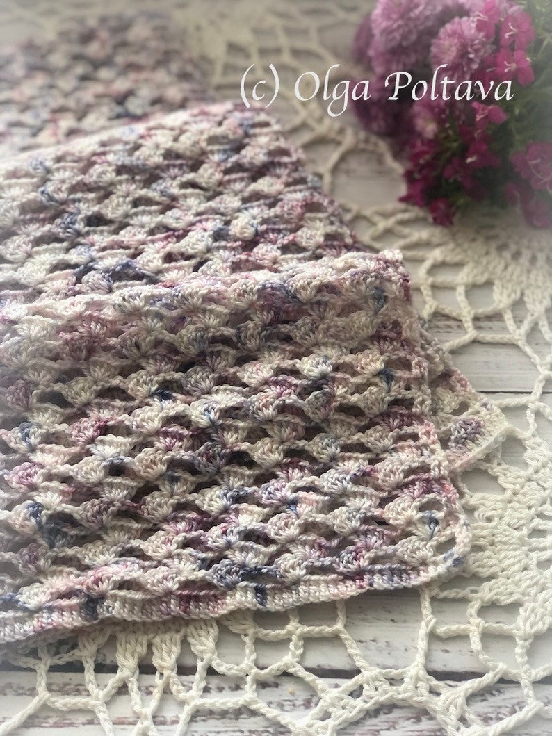 Pu&ograve; includere: Uno scialle all'uncinetto in tonalit&agrave; di bianco, rosa e viola con un delicato motivo a pizzo. Lo scialle &egrave; appoggiato su un pizzo all'uncinetto bianco. (c) Olga Poltava