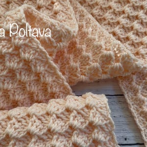 May include: A peach-colored, crocheted scarf with a textured, raised pattern. The scarf is folded and draped, showcasing the intricate stitch work. The text "(c) Olga Poltava" is visible in the upper left corner. The scarf appears soft and warm.