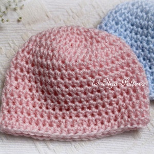 May include: A close-up of two handmade crochet baby hats. The front hat is light pink, and the second hat is light blue. The hats are made with a textured stitch pattern. The copyright text "(c) Olga Poltava" is visible on the pink hat.