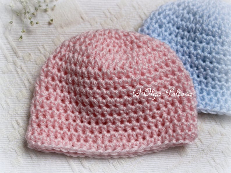 May include: A close-up of two handmade crochet baby hats. The front hat is light pink, and the second hat is light blue. The hats are made with a textured stitch pattern. The copyright text "(c) Olga Poltava" is visible on the pink hat.