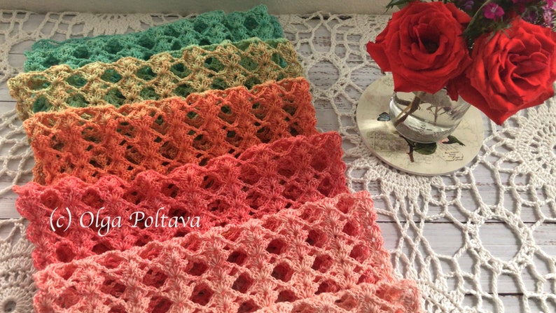 Pode incluir: Uma pilha de faixas de cabelo de croch&ecirc; feitas &agrave; m&atilde;o em tons de verde, p&ecirc;ssego e rosa. As faixas est&atilde;o dispostas sobre uma toalha de croch&ecirc; branca. Um pequeno vaso com rosas vermelhas &agrave; direita.