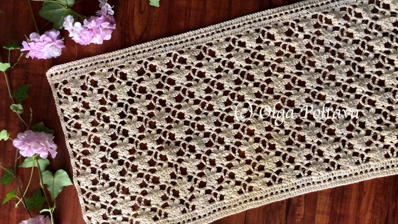 May include: A crocheted table runner with a delicate floral pattern in a cream color. The runner is made with a fine yarn and has a delicate lace border.