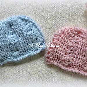 May include: Two handmade crochet baby hats, one light blue and one pink, with a textured floral pattern. The hats are displayed on a white surface with floral accents. The text "(c) Olga Poltava" is visible on the hats.