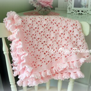 May include: A pink crocheted baby blanket with a lacy design and ruffled edges. The blanket is draped over a white chair.