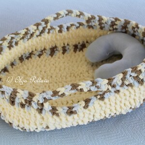 May include: A crocheted basket with brown, blue, and white yarn. The basket has two handles and a light blue pillow inside.