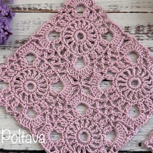 May include: A square, crocheted doily in a dusty rose color, featuring a floral pattern with circular and star-like elements. A small, matching doily is next to it. A skein of yarn and purple flowers are also in the image.