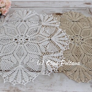 May include: Two crocheted doilies, one white and one beige, with a delicate floral pattern. The doilies are laid out on a whitewashed wooden surface.
