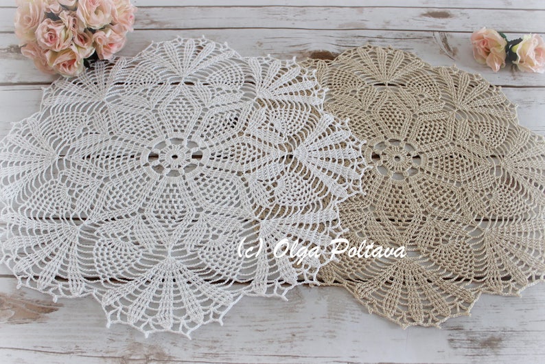 May include: Two crocheted doilies, one white and one beige, with a delicate floral pattern. The doilies are laid out on a whitewashed wooden surface.