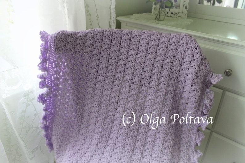 May include: A lavender crochet baby blanket with a delicate lace border. The blanket is draped over a white dresser with a floral arrangement on top. (c) Olga Poltava