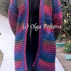 May include: A long, open-front crochet cardigan in a mix of colors including blue, purple, brown, and red. The textured knitwear features a ribbed design and pockets. The text "(c) Olga Poltava" is visible on the garment.