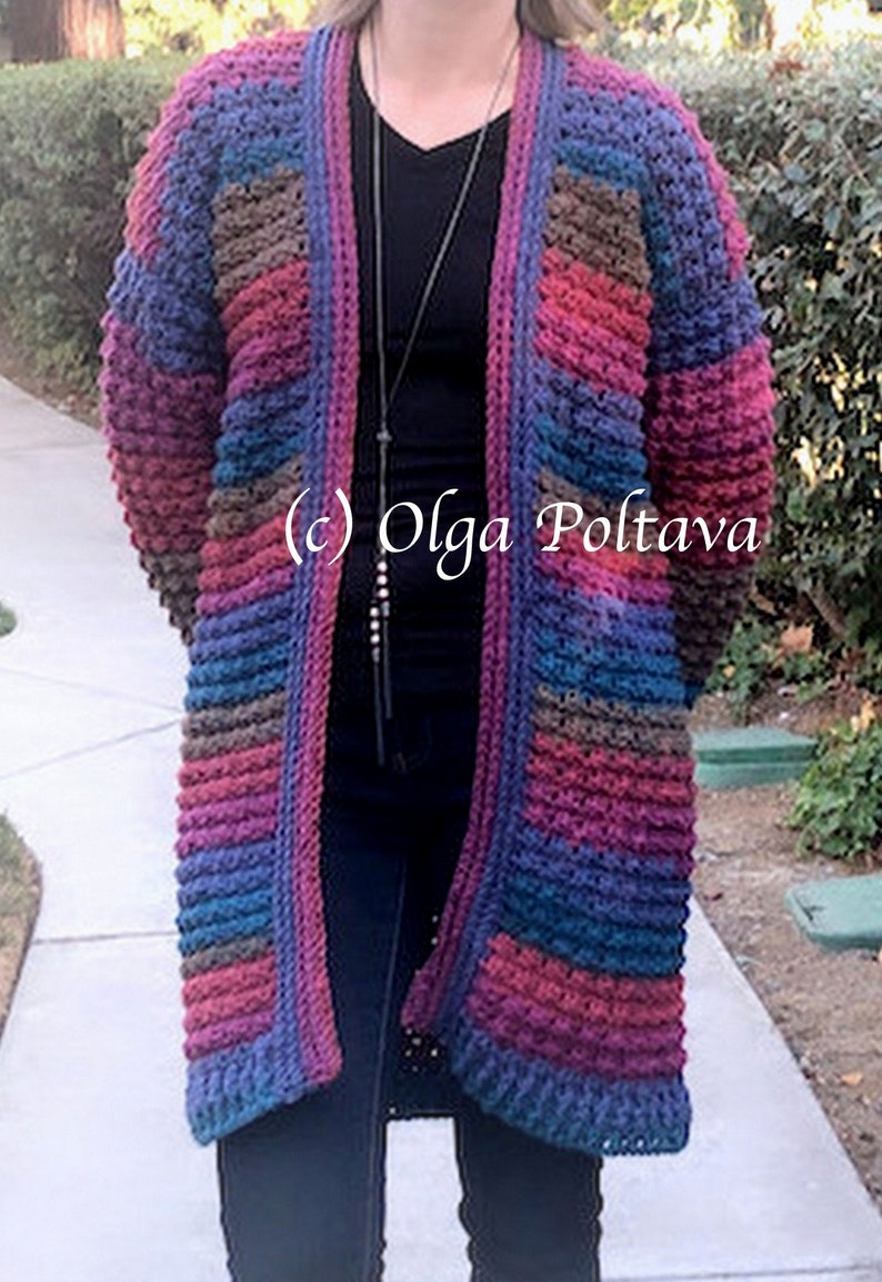May include: A long, open-front crochet cardigan in a mix of colors including blue, purple, brown, and red. The textured knitwear features a ribbed design and pockets. The text "(c) Olga Poltava" is visible on the garment.