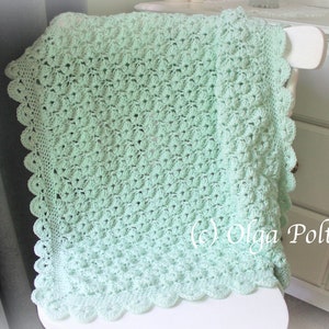 May include: A mint green crocheted blanket with a scalloped edge is draped over a white chair. The blanket features a textured pattern and is made of soft yarn. The blanket is a handmade item, perfect for a baby or as a decorative piece.