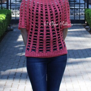 May include: A coral-colored, open-weave crochet top with short sleeves. The top has a boat neck and a loose, airy design. The model is wearing dark blue jeans. The text "(c) Olga Poltava" is visible on the top.