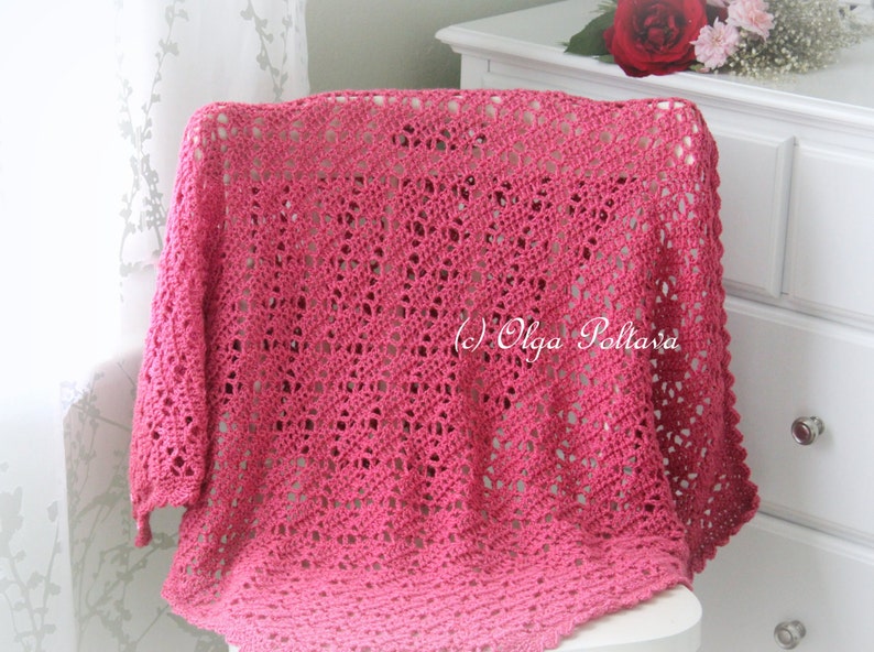 May include: A pink crocheted shawl with a delicate openwork pattern. The shawl is draped over a white chair and has a fringe border.