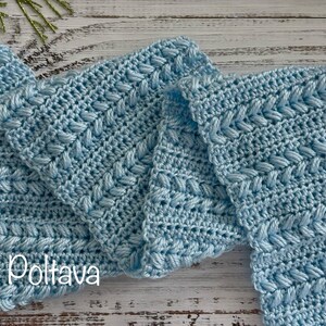 May include: Light blue crocheted scarf with a textured pattern. The scarf is made of soft yarn and has a detailed stitch design. The image shows several folded sections of the scarf, showcasing the intricate craftsmanship.