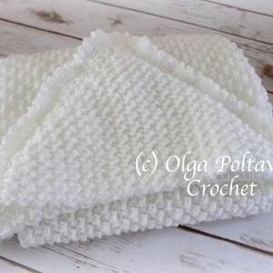 May include: White crocheted baby blanket with a ruffled edge. The blanket is folded in half and lying on a white wooden surface. (c) Olga Poltava Crochet